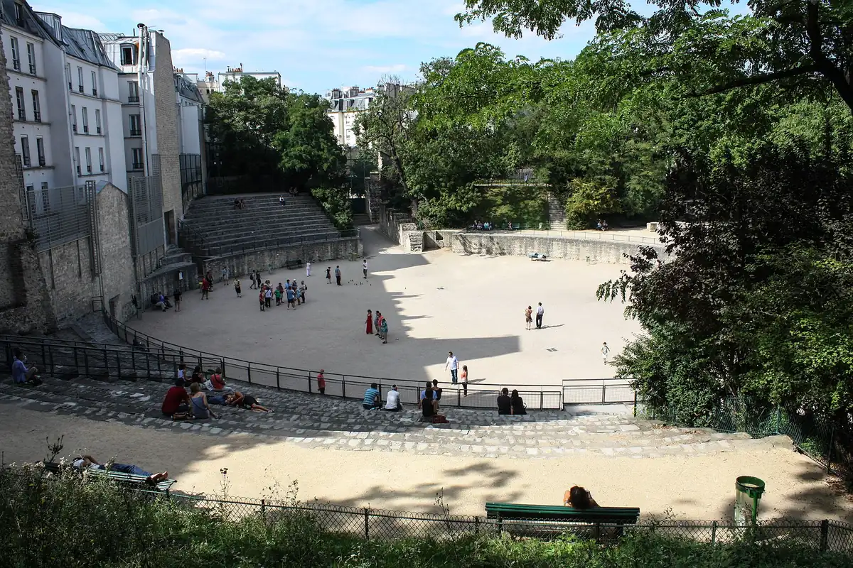 Les arènes de Lutèce, une piste de sable entourée de gradins de pierre et d'arbres, avec des joueurs de pétanque